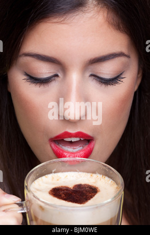 Frau, trinken einen Cappuccino Kaffee mit einer Liebe Herzen Form besprenkeln an der Spitze. Stockfoto