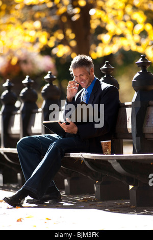 Geschäftsmann auf Holzbank im Freien mit Zeitung Stockfoto