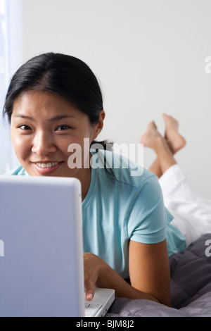 Frau auf dem Bett mit Laptop und Handy Stockfoto