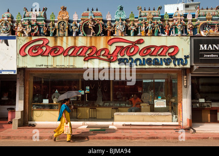 Indien, Kerala, Alappuzha (Alleppey), YMCA Road, Frau mit Sonnenschirm, vorbei an Geschäften unter bunte kleine Hindu-Tempel Stockfoto