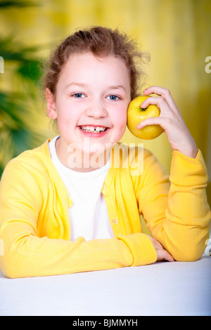 8 Jahre altes Mädchen an einem Tisch mit einem Apfel Stockfoto