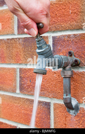 Großbritannien, UK, Europa. Person einschalten Wasser auf einen Wasserhahn an einer Mauer befestigt Stockfoto