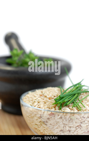 Frisch gepflückt Oregano und Rosmarin in einem grauen Mörser und eine Schüssel Vollkorn-Reis mit frischem Schnittlauch auf einem Holzbrett Stockfoto