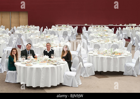 Gruppe von jungen Leuten an einem Tisch in einem leeren Raum des Restaurants sitzen. Bedeckt mit einer weißen Tischen rund um Stockfoto