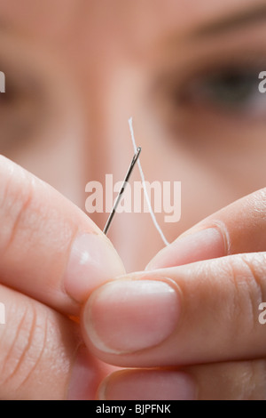 Eine Frau, die Baumwolle durch eine Nadel einfädeln Stockfoto