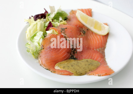 Geräucherter Lachs, Salat, Zitrone und Sauce auf einem Teller. Stockfoto