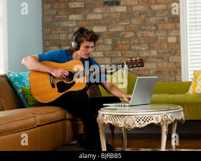 USA, Utah, Provo, junge Mann spielt Gitarre, mit Laptop im Wohnzimmer Stockfoto