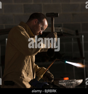USA, Utah, Orem, Mann mit Hammer und Lötlampe in Werkstatt Schweißen Stockfoto