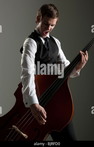 Junger Mann spielt Kontrabass wie eine Gitarre, Studio gedreht Stockfoto