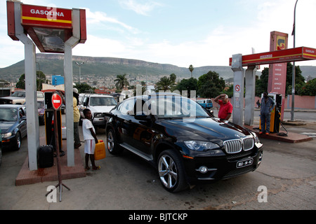 Angolanischen Elite genießen die Einfuhr von teuren Autos, während die Armen schauen auf der Warteliste, um ihre Behälter mit Kraftstoff füllen. Stockfoto