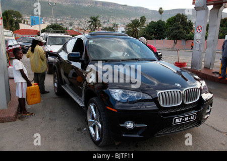 Angolanischen Elite genießen die Einfuhr von teuren Autos, während die Armen schauen auf der Warteliste, um ihre Behälter mit Kraftstoff füllen. Stockfoto