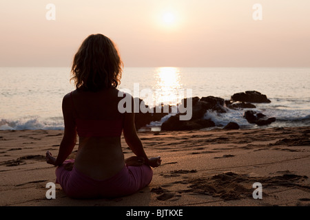 Frau praktizieren Yoga am Strand bei Sonnenuntergang Stockfoto