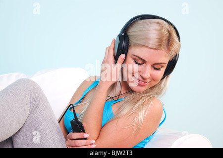 Junge, blonde Frau saß in einem Sessel, anhören von Musik auf ihrem MP3-Player über Kopfhörer