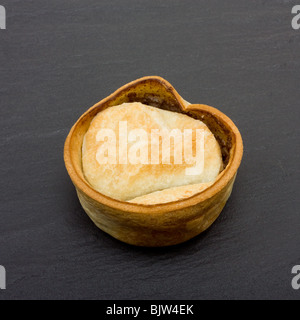 Kleine Runde schottischen Stil Steak und Soße Pie dunklen Schiefer Hintergrund isoliert. Stockfoto