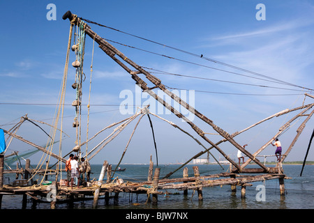 Indien, Kerala, Kochi, Fort Cochin, Männer, die auf chinesischen Fischernetzen Stockfoto