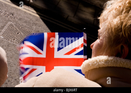Eine Frau Union Jack Flagge weht im Wind wie sie mit Spannung das Aussehen der Queen erwartet. Stockfoto