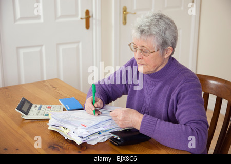 Ältere Frau Rentner zahlt eine Rechnung mit einem großen Haufen von Stromrechnungen auf einem Tisch mit einer Kreditkarte zu zahlen, um Schulden. England Großbritannien Stockfoto