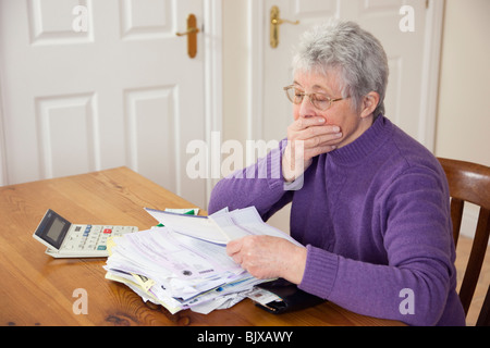 Ältere Frau Rentner mit einem großen Stapel von Rechnungen auf eine Tabelle mit der Hand über den Mund in großer Rat Steuern in Zeiten der Sparpolitik UK schockiert Stockfoto