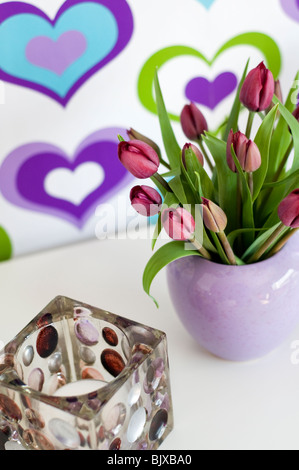 Eine Vase mit violette Tulpen vor bunten Tapete verziert mit einem Herz-Muster Stockfoto