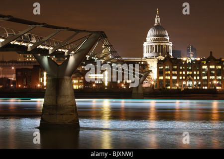 St. Pauls Cathedral mit Millennium Bridge und der Themse im Vordergrund in der Nacht. Lichtspuren von vorbeifahrenden Flussschiff. Stockfoto