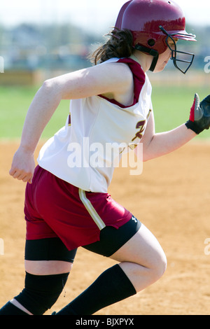 Extreme Nahaufnahme von einem High-School-Mädchen laufen die Grundlagen in einem Softball-Spiel. Sie ist in Uniform mit Helm und einen Handschuh. Stockfoto