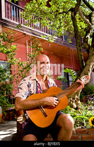 Porträt von lächelnden jungen Mann spielt Gitarre im Innenhof Stockfoto
