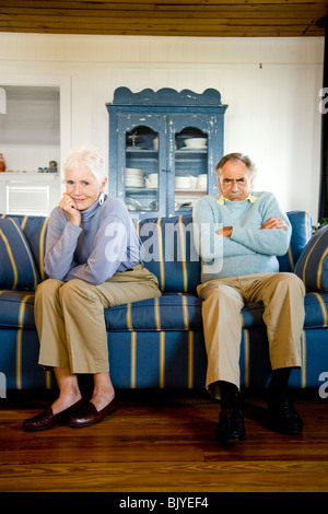 Älteres Paar auf Couch sitzen, hartnäckige Mann amüsiert Frau Stockfoto