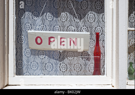 Eine alte weiß getünchten Fenster mit einem Schild "geöffnet" hängen vor Spitzen Vorhänge in Lincoln, New Mexico. Stockfoto
