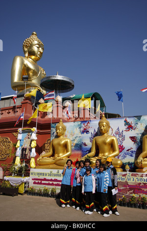 Schülerinnen und Schüler posieren vor einem riesigen goldenen Buddha im Sop Ruak, The Golden Triangle, durch den Mekong im Norden Thailands Stockfoto