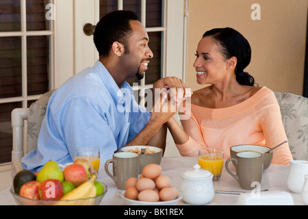 Ein glückliches afroamerikanische Mann und Frau-Paar in den Dreißigern, die Hand in Hand und mit einem gesunden Frühstück draußen Stockfoto
