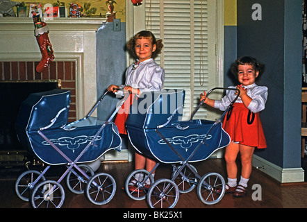 Zwei Mädchen posieren mit ihrem neuen Spielzeug Kinderwagen zu Weihnachten in den USA in den 1950er Jahren Stockfoto