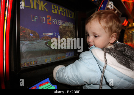 Ein junges Baby junge; nur ein Jahr alt unterhalten sich durch das Spielen auf ein Auto-Rennspiel in der Spielhalle in Skegness Stockfoto