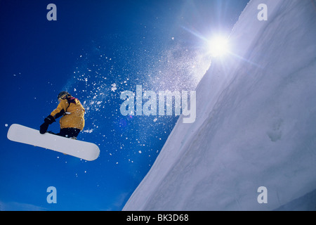 Mann auf einem Snowboard mit der Sonne über die Schulter in den Wasatch Mountains von Norden Utahs durch die Luft fliegen. Stockfoto