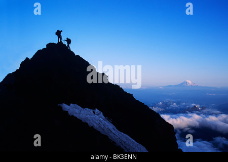 Zwei Bergsteiger am Gipfel der Turmspitze auf Mount Rainier in Mount Rainier Nationalpark, Washington. Mount Adams am Horizont. Stockfoto