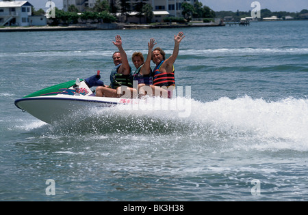 Drei Personen, die Schwimmwesten (persönliche Schwimmvorrichtungen) tragen und winken, während sie einen Jet Ski fahren in der US-amerikanischen Bundesstaat Florida Stockfoto