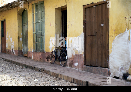 Straßenszene mit einem Fahrrad und zwei Kindern in einer Tür der kolonialen Struktur, die in der Stadt Trinidad, Kuba, in Verfall ist Stockfoto
