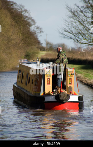 junger Mann mit Hund Lenkung schmale Grachtenboot auf Trent und Mersey Kanal am Stein Stockfoto