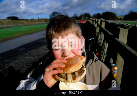 Stock Foto des jungen in einen Burger beißen gekauft von einem Straße Seite Café. Stockfoto