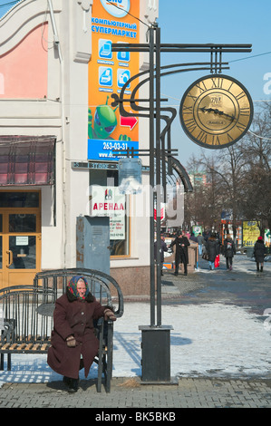 Einsame ältere Frau sitzen auf Bank in der Nähe einer Straße Uhr. Tscheljabinsk, Russland. Winterzeit Stockfoto