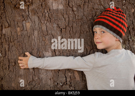 Jungen tragen Mütze Baumstamm umarmen Stockfoto