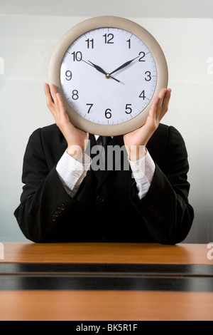 Unternehmer, die eine Uhr vor seinem Gesicht halten Stockfoto