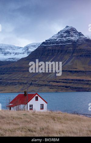 Haus mit roten Dächern und schneebedeckte Berge in Reydarfjördur Fjord, Osten Fjorde, Island, Polarregionen Stockfoto