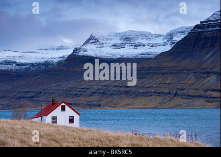 Haus mit roten Dächern und schneebedeckte Berge in Reydarfjördur Fjord, Osten Fjorde, Island, Polarregionen Stockfoto