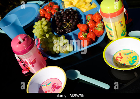 Im Freien essen oder ein Picknick auf einem schwarzen Tisch mit blauen Kunststoff Schüsseln, Tassen und Krüge mit Obst und Salat Stockfoto