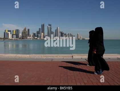 Zwei arabische Frauen zu Fuß auf der Corniche mit West Bay Skyline von Doha im Hintergrund. Stockfoto