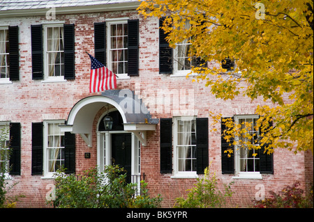 Ein altes Backsteinhaus zeigt eine amerikanische Flagge und umgeben von Herbstlaub in Townshend, Vermont, USA Stockfoto