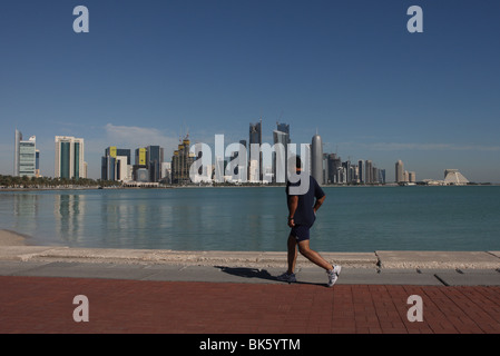 Mann Joggen entlang der Corniche mit West Bay Skyline von Doha im Hintergrund. Stockfoto