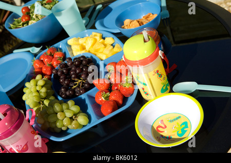 Im Freien essen oder ein Picknick auf einem schwarzen Tisch mit blauen Kunststoff Schüsseln, Tassen und Krüge mit Obst und Salat Stockfoto