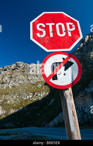 Ein Stop-Schild und ein Recht machen verbotene Zeichen mit Einschusslöchern, mit einem felsigen Hügel im Hintergrund. Aus Südafrika. Stockfoto