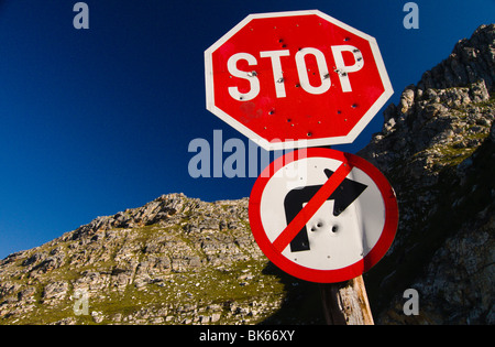 Ein Stop-Schild und ein Recht machen verbotene Zeichen mit Einschusslöchern, mit einem felsigen Hügel im Hintergrund. Aus Südafrika. Stockfoto